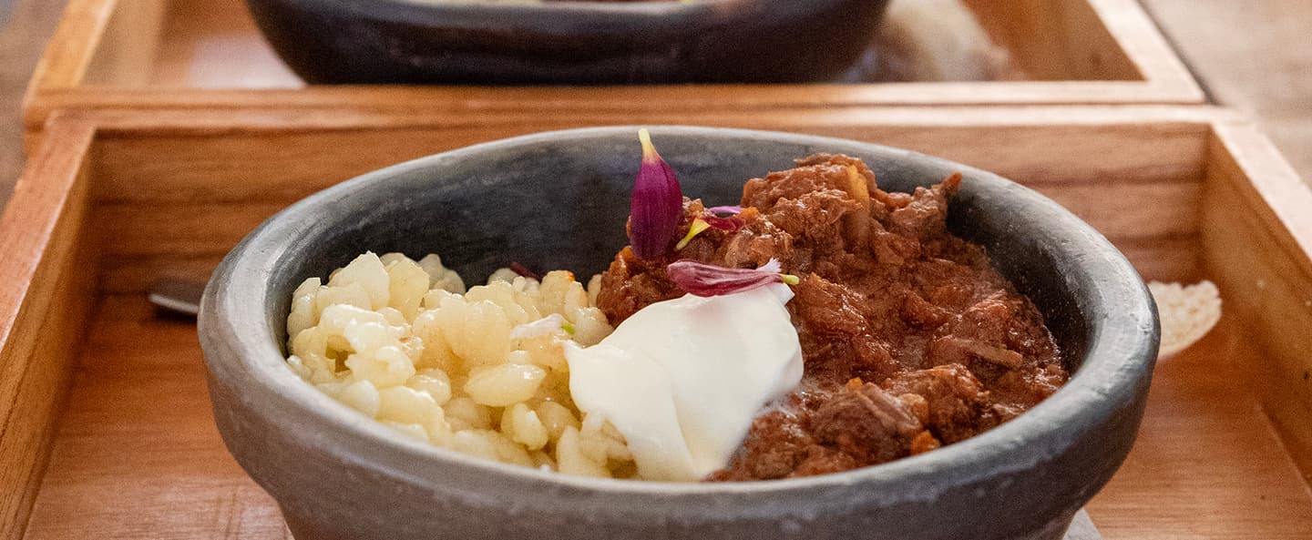 Guiso servido en cazuela de piedra con crema y flores comestibles